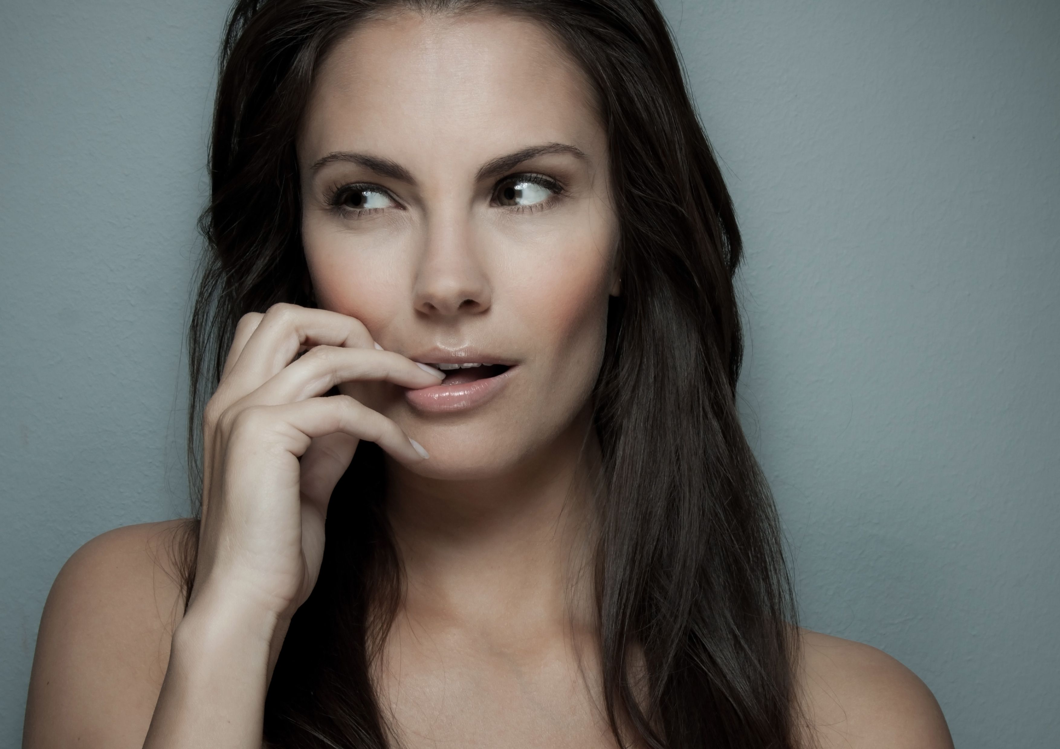 Beautyporträt einer Frau mit langem dunklem Haar und natürlichem Make-up, Finger an den Lippen