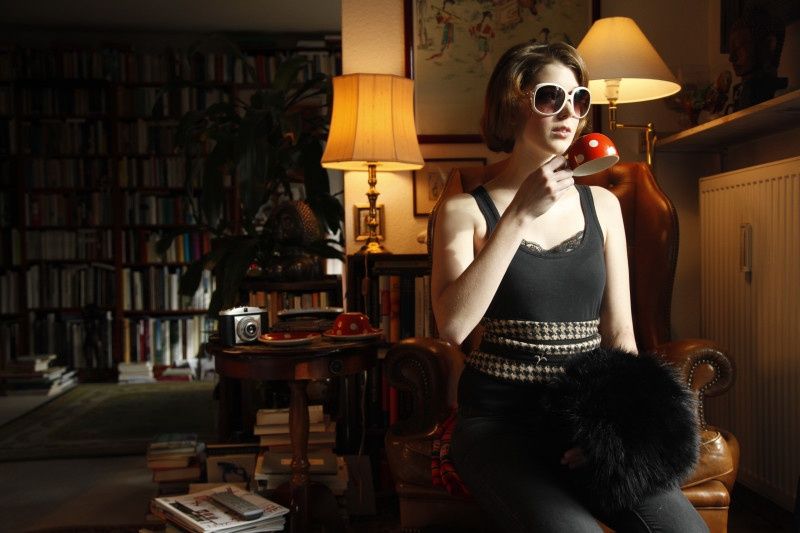 Model mit weißer Sonnenbrille in einem Ledersessel vor Bücherregalen