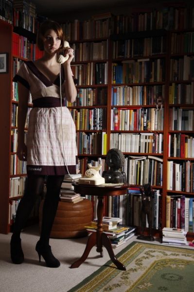 Model in Rock und Strumpfhose telefoniert vor einer Bücherwand