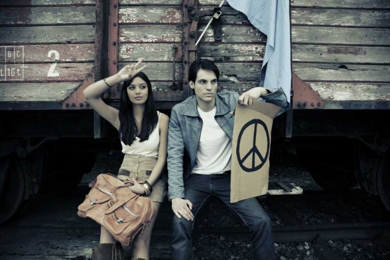 Hippie-Paar mit Peace-Schild und Ledertasche vor einem Güterwaggon