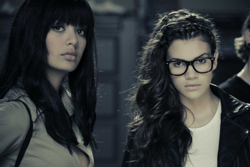 Zwei Models mit langem dunklem Haar, eines mit schwarzer Brille, im Editorial-Look
