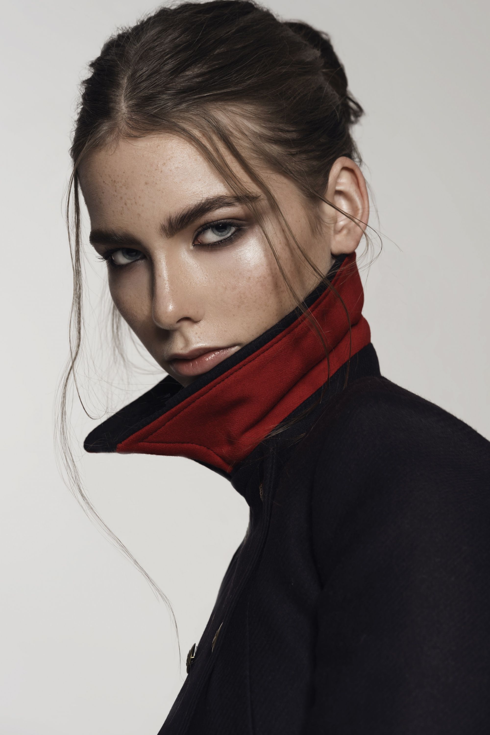Model mit Smokey Eyes und zurückgestecktem Haar im schwarzen Mantel mit rotem Kragen