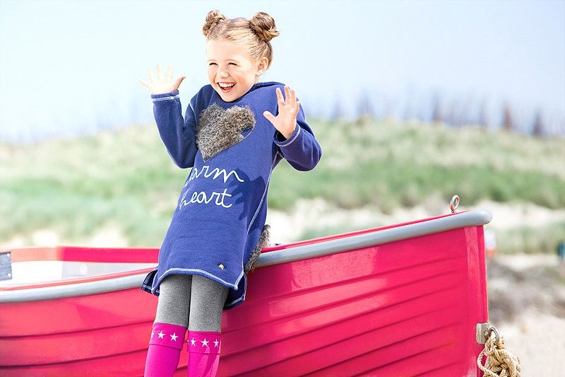 Mädchen im blauen Kleid steht in einem roten Boot am Strand
