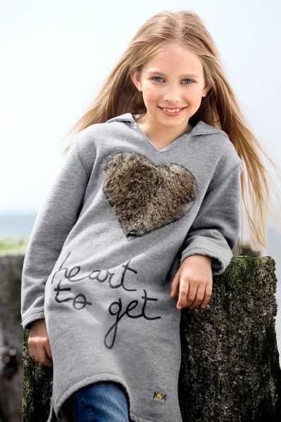 Mädchen mit langem blondem Haar im grauen Herzpullover am Strand