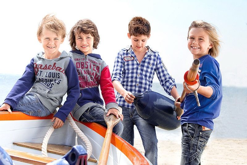 Vier Jungen in Kapuzenpullis und Hemden mit Ruderboot am Strand